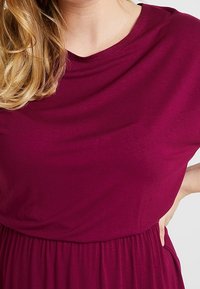 Abito a maniche corte in tessuto magenta intenso, caratterizzato da scollo drappeggiato e vita arricciata, con una texture liscia e morbida.