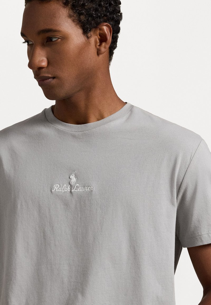 Maglietta in cotone grigio chiaro con maniche corte, con un sottile logo ricamato e il nome del marchio sul lato sinistro del petto. Design classico con scollo rotondo.