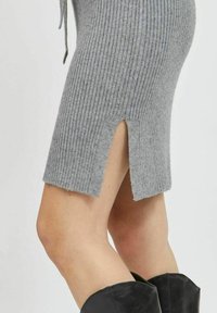 Abito a maglia grigio a coste con taglio di lunghezza media e spacco laterale. Presenta una texture morbida e un design aderente, abbinato a stivali neri al ginocchio.