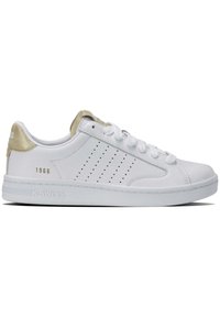 White leather sneaker with gold accents, perforated side design, flat white laces, and solid rubber sole. Branding on heel and side.
