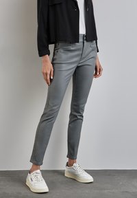 Grå slim-fit byxor i stretchmaterial med en slät yta. I kombination med vita sneakers som har svarta och grå detaljer.