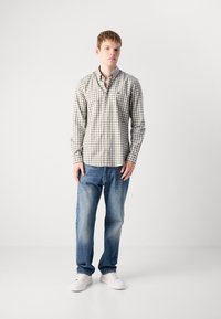 Camicia a maniche lunghe a righe beige e marrone, abbinata a jeans blu sbiaditi e sneakers bianche. Design semplice, vestibilità casual.