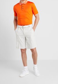 Camisa polo naranja con un cuello en contraste, pantalones cortos blancos y zapatillas blancas. Textura suave, ajuste casual. Detalles de diseño simples.