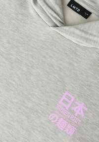 Svetlo siva majica z majhnim roza grafikonom z napisom "Ramen Ramen Ramen japonska rezanci" in japonskimi znaki spredaj.