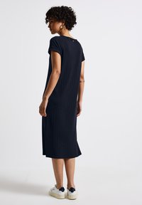 Schwarzes geripptes Midikleid mit kurzen Ärmeln, rundem Ausschnitt, seitlichen Schlitzen und lässiger Passform, kombiniert mit weißen Sneakers.