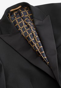 Schwarze Blazer mit satinierter Fütterung und goldenem, kreisförmigem Kettenmuster. Mit Reverskragen, taillierter Passform und glatter Oberfläche.