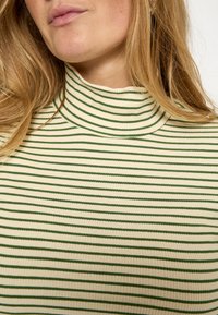 Jersey de cuello alto a rayas verdes y crema con textura acanalada. El cuello es alto y ajustado, resaltando el diseño ceñido al cuerpo.