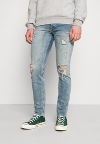 Ljusblå slitna jeans med rivna detaljer vid knäna, kombinerat med gröna högklackade sneakers. Materialet är denim med en urtvättad finish.
