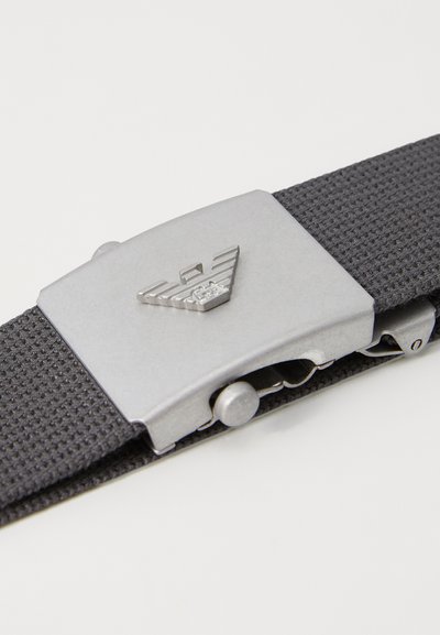 Gray textile belt with a silver metal buckle featuring a logo and a textured design. The buckle has a sliding mechanism for adjustment.