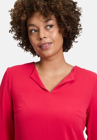 Helle pinkfarbene Bluse mit V-Ausschnitt und langen Ärmeln. Glatte Textur, einfaches Design und bequeme Passform, geeignet für Freizeit- oder Arbeitsumgebungen.
