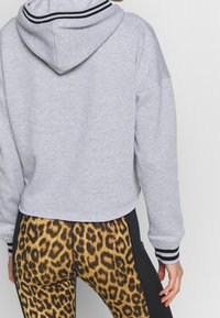 Felpa grigia corta con cappuccio regolabile, caratterizzata da accenti a righe bianche e nere sui polsini. Abbinata a leggings con stampa leopardata.