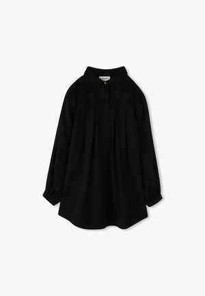 Blouse noire à manches longues avec un col structuré, présentant un empiècement avant orné de broderies en zigzag et des détails froncés au niveau des manches.