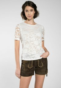 Weißes Spitzent-Shirt mit floralen Mustern, kurzen Ärmeln und rundem Ausschnitt. Kombiniert mit braunen Shorts mit Stickerei und gelben Akzenten.
