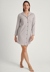 Camicia da notte con design a bottoni, maniche lunghe e tessuto bianco con un motivo a onde nere. Texture morbida, lunghezza al ginocchio.