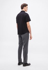 Μαύρο πόλο πουκάμισο με κοντά μανίκια συνδυασμένο με γκρι παντελόνι με ραφές. Το σύνολο διαθέτει ομαλή υφή και κλασικό σχέδιο. Μαύρα παπούτσια ολοκληρώνουν την εμφάνιση.