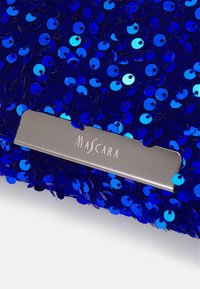 Niebieska tkanina z cekinami z srebrną prostokątną metką wygrawerowaną słowem "MASCARA" w eleganckim kroju pisma.