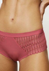 Roze kleurige slip met een glad satijnen voorkant en een delicate kanten overlay met een cirkelpatroon langs de taille.