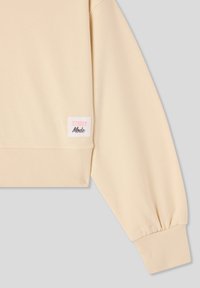 Felpa beige con polsini e orlo a costine, con un'etichetta "STREET Mode" in rosa e nero sul lato. Tessuto morbido.