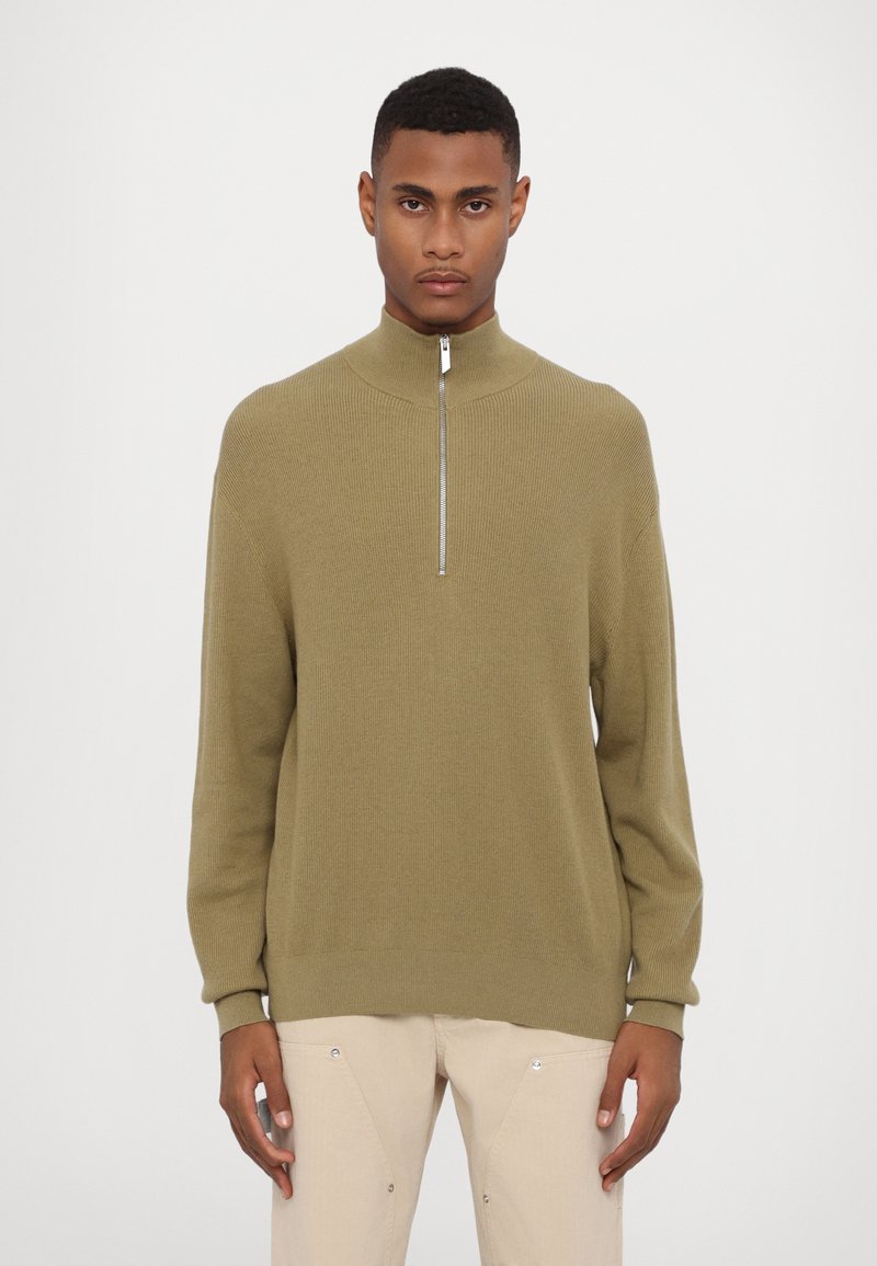 Olive green knit sweater with a high collar and quarter zipper. Loose fit, ribbed texture, long sleeves, and a straight hem.