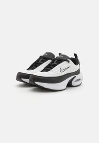 Witte en zwarte sportschoenen met een gestructureerde bovenkant, ronde neus, zwarte veters en een gevoerde zool met zichtbare luchtunit. Nike-logo aan de zijkant.