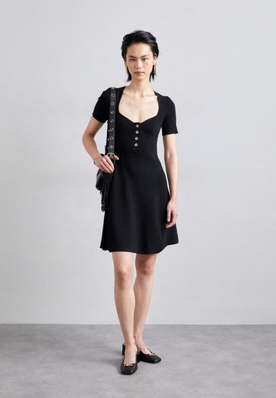 Rochie scurtă neagră cu mâneci scurte, decolteu rotund, textura raibată, detalii cu nasturi pe față și fustă evazată. Asortată cu încălțăminte neagră.