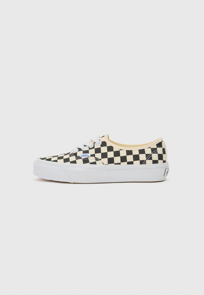 Black and white checkerboard canvas sneakers with a lace-up design, white rubber sole, and tan interior accents. Brand logo present on side.