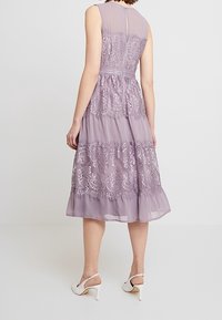 Lavendelfärgad klänning med spetsdetaljer, ärmlös design, rynkad midja, lager-skjorta och en dold dragkedja bak. Kombinerad med vita klackar.