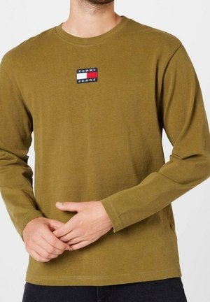 Langärmeliges T-Shirt aus olivgrünem Baumwollstoff mit Rundhalsausschnitt, versehen mit einem kleinen schwarzen, roten und weißen "TOMMY JEANS"-Logo auf der Brust.
