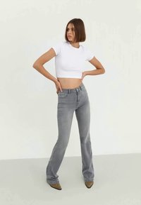 Šedé rozšířené džíny vyrobené z denimu, s klasickým designem pěti kapes a jemným vyblednutím, v kombinaci s krátkým bílým tričkem.