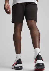 Pantalones cortos deportivos de color marrón oscuro con una textura suave, acompañados de calcetines blancos y zapatillas con acentos en negro, rojo y blanco.
