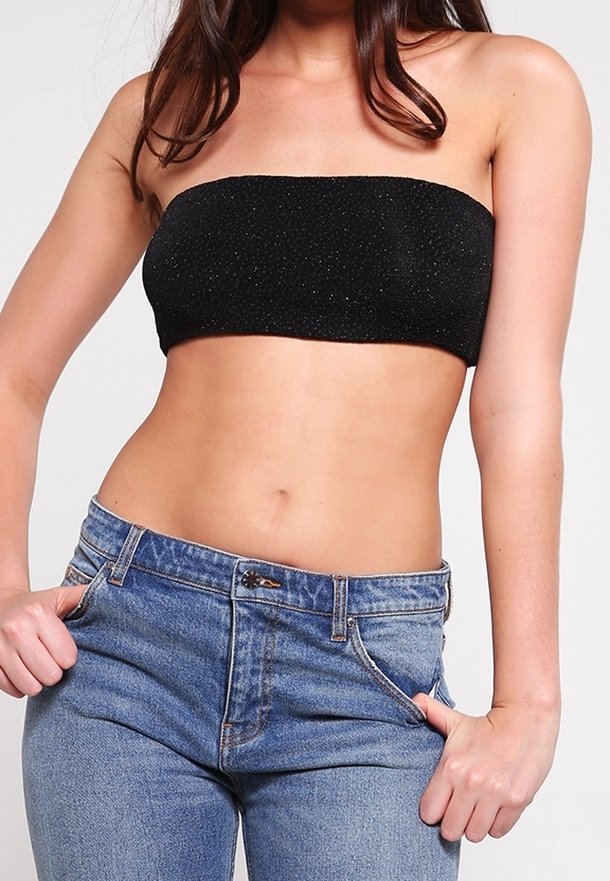 Femme portant un crop top noir sans bretelles et un jean taille haute bleu, les mains tenant la ceinture dans une pose décontractée.