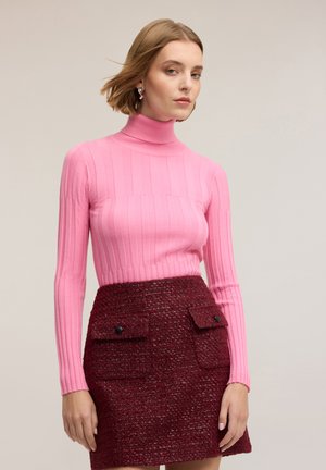 Różowy prążkowany sweter z golfem i długimi rękawami, zestawiony z bordową spódnicą o fakturze, z dwoma przednimi kieszeniami i czarnymi guzikami.