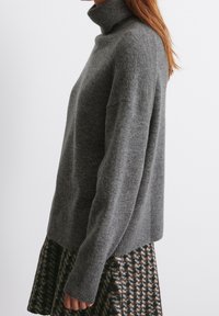 Harmaa pooloneule, valmistettu pehmeästä villasta, rento istuvuus ja pitkät hihat, yhdistetty kuvioituun hameeseen, jossa on tummia ja vaaleita sävyjä.