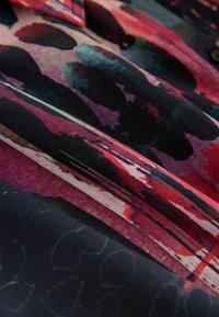 Záhyby látky s abstraktnými čiernymi, červenými, ružovými a modrými ťahmi štetca vytvárajú vrstvenú, farebnú textilnú textúru.