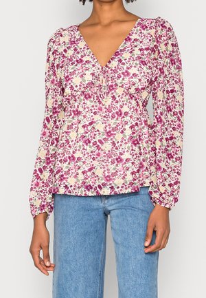 Mujer con una blusa de manga larga con estampado floral en tonos rosa, blanco y verde, combinada con vaqueros azul claro.