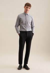 Camicia grigia con colletto, abbinata a pantaloni neri aderenti e scarpe nere. Tessuto liscio con una leggera lucentezza, senza motivi visibili.