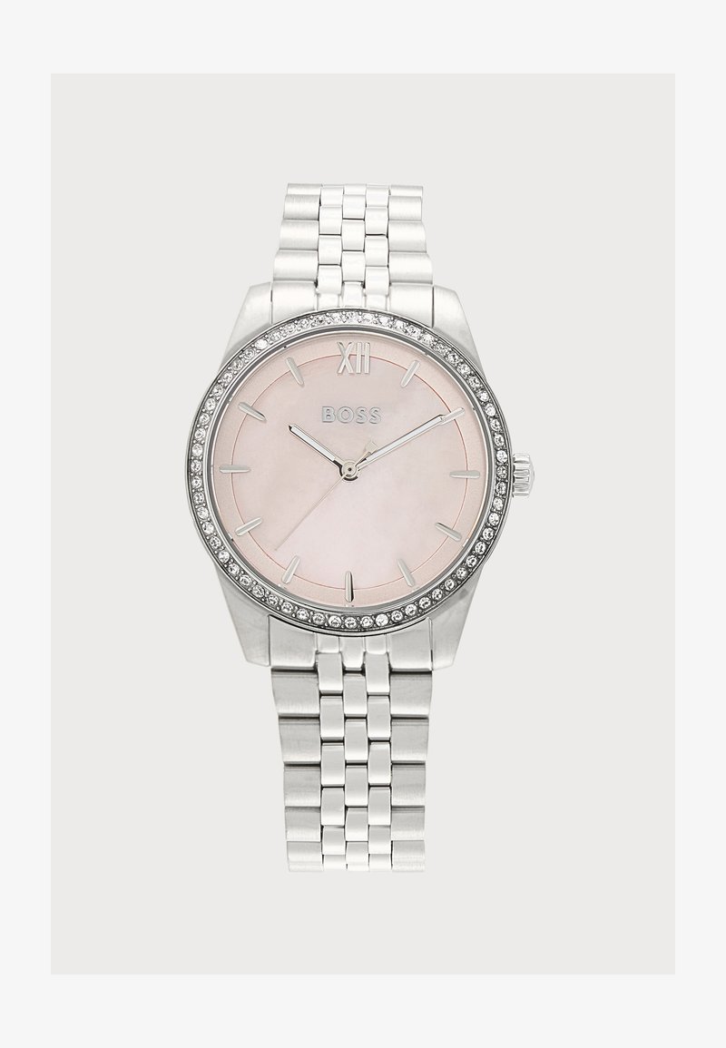 Montre-bracelet argentée avec cadran rose, lunette ornée de cristaux, index des heures argentés et bracelet à maillons métalliques, affichant l'heure 10:10:10.