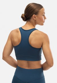 Sujetador deportivo azul oscuro con diseño de tirantes cruzados. Fabricado en tejido suave, presenta costuras en contraste y una silueta ajustada.