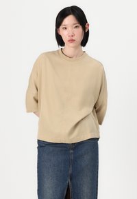 Beige cotton t-shirt with a round neckline, short sleeves, and relaxed fit, paired with a dark denim skirt featuring a front slit.