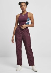 Bordo urheilullinen crop-top, jossa on turkoosi yksityiskohta, yhdistettynä bordoon, löysiin verkkohousuihin. Valkoiset kengät täydentävät asun.