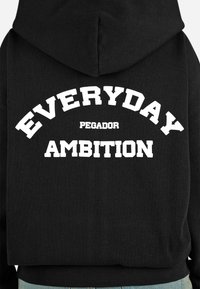 Felpa nera con cappuccio caratterizzata da un grande design di testo bianco sul retro, che recita "EVERYDAY PEGADOR AMBITION" in caratteri bold e sportivi.