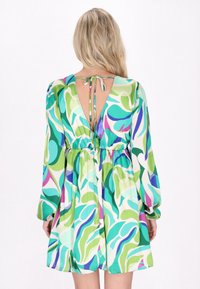 Rochie colorată cu un decolteu adânc în spate, mâneci lungi și talie cu șnur. Materialul are modele abstracte de frunze verzi și purpurii.