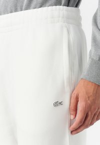 Witte fleece joggingbroeken met een elastische tailleband, zijzakken en een klein grijs geborduurd krokodillenlogo op de dij.