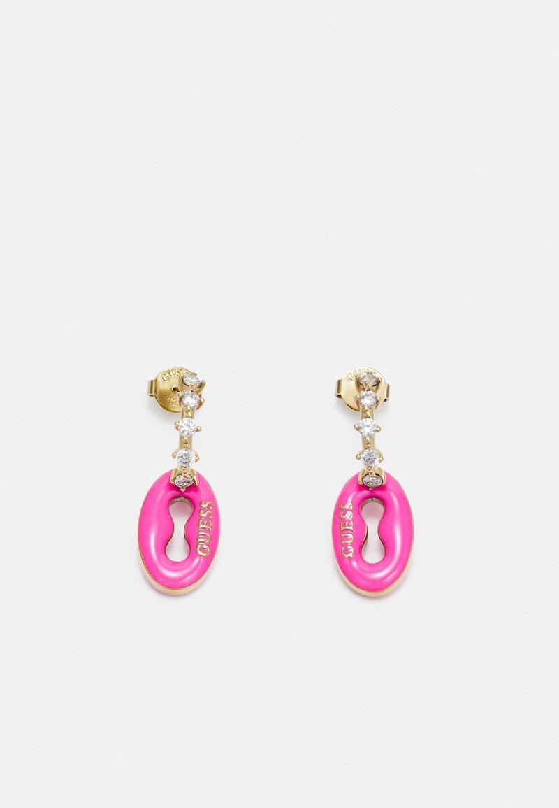 Boucles d'oreilles dorées avec trois pierres précieuses claires surmontant des pendentifs ovales roses gravés du mot "GUESS" et un trou en forme de serrure au centre.