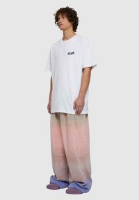 Fehér, túlméretezett póló, amelyen a "bulizzunk" felirat látható. Laza, több színű, gradient széles szárú nadrág, amely rózsaszínről lila színre vált, lila papucsokkal viselve.