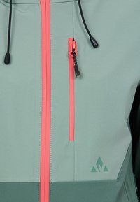 Veste vert clair avec une texture lisse, dotée d'une fermeture éclair centrale avec des accents roses, d'une poche zippée sur le côté et d'un logo discret près de l'ourlet.