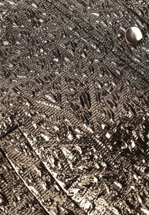 Metalen goudkleurige stof met een gestructureerd geometrisch patroon en een metalen knoopdetail, met plooien en een gladde glans.