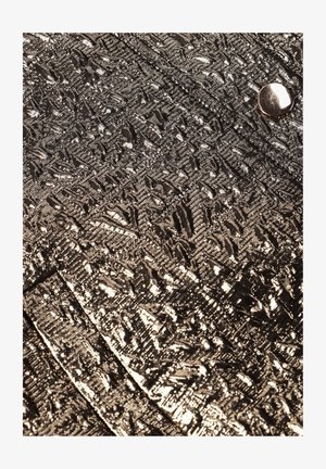 Metalen goudkleurige stof met een gestructureerd geometrisch patroon en een metalen knoopdetail, met plooien en een gladde glans.