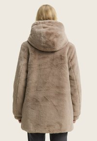 Faux-Fur-Mantel in hellem Beige mit großer Kapuze, locker geschnitten und mit strukturierter Oberfläche. Einfaches Design ohne sichtbare Beschläge.