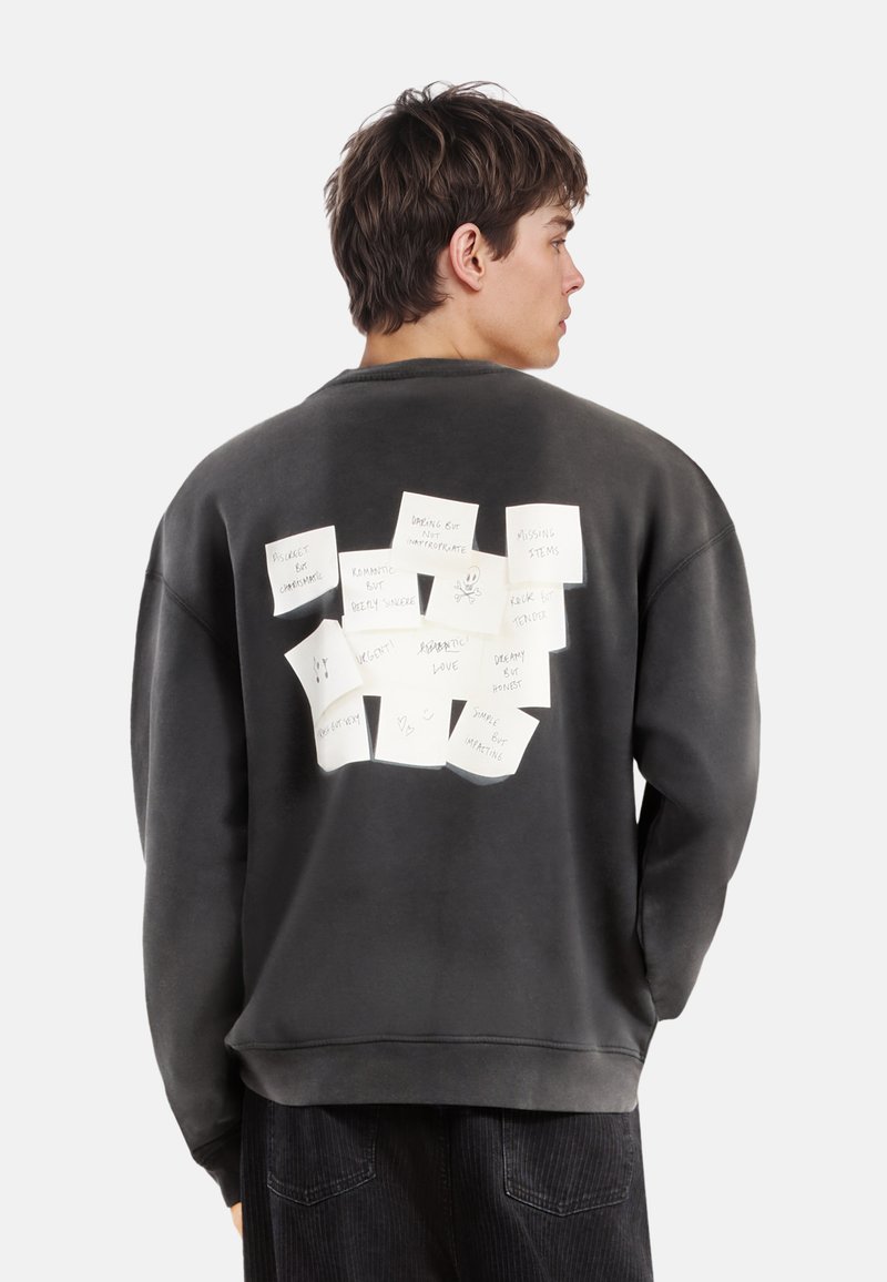 Donkergrijze sweatshirt met een ontspannen pasvorm, voorzien van witte notities en krabbels op de achterkant. Zachte stof en geribde manchetten.